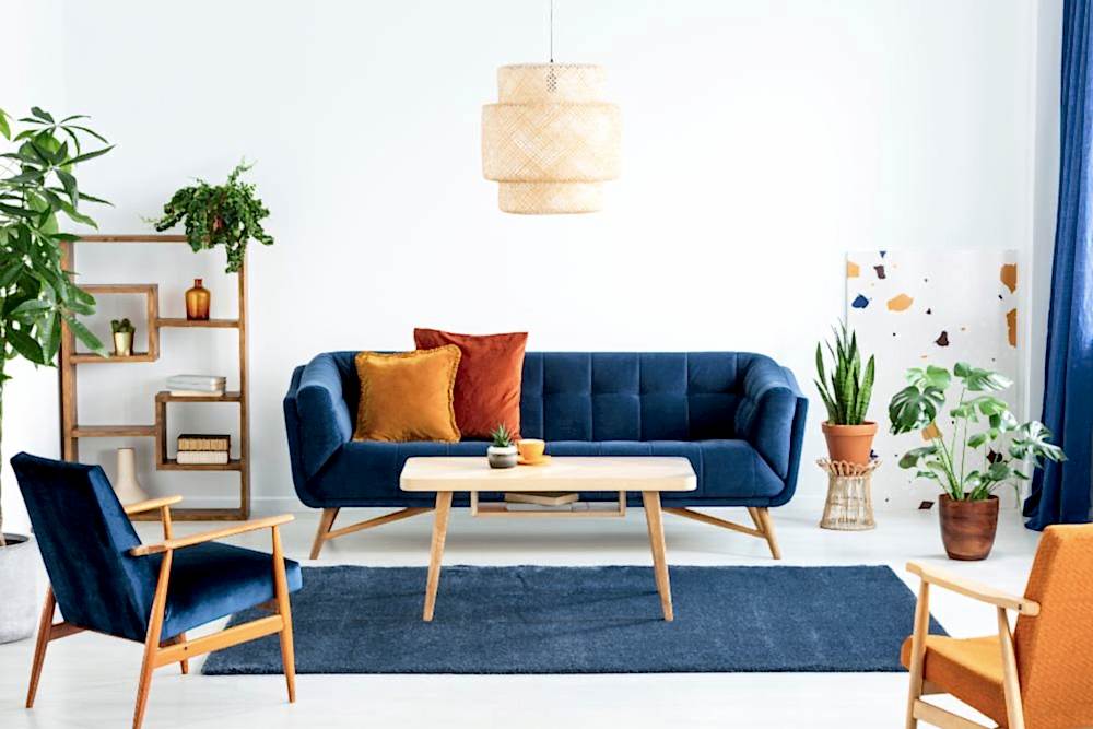 Mavi koltuklar, renkli kırlentler, ahşap avize, kitaplık ve saksıda yeşil bitkilerle renkli oturma odası dekorasyonu